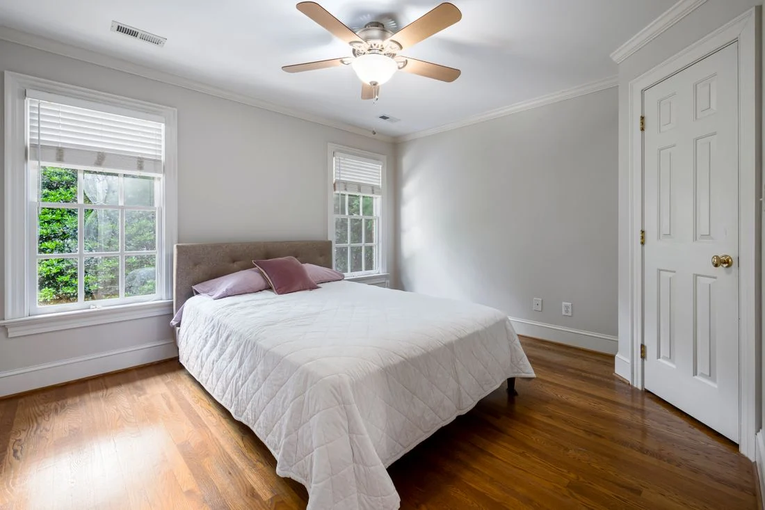 Bed positioned between two windows in a bright room