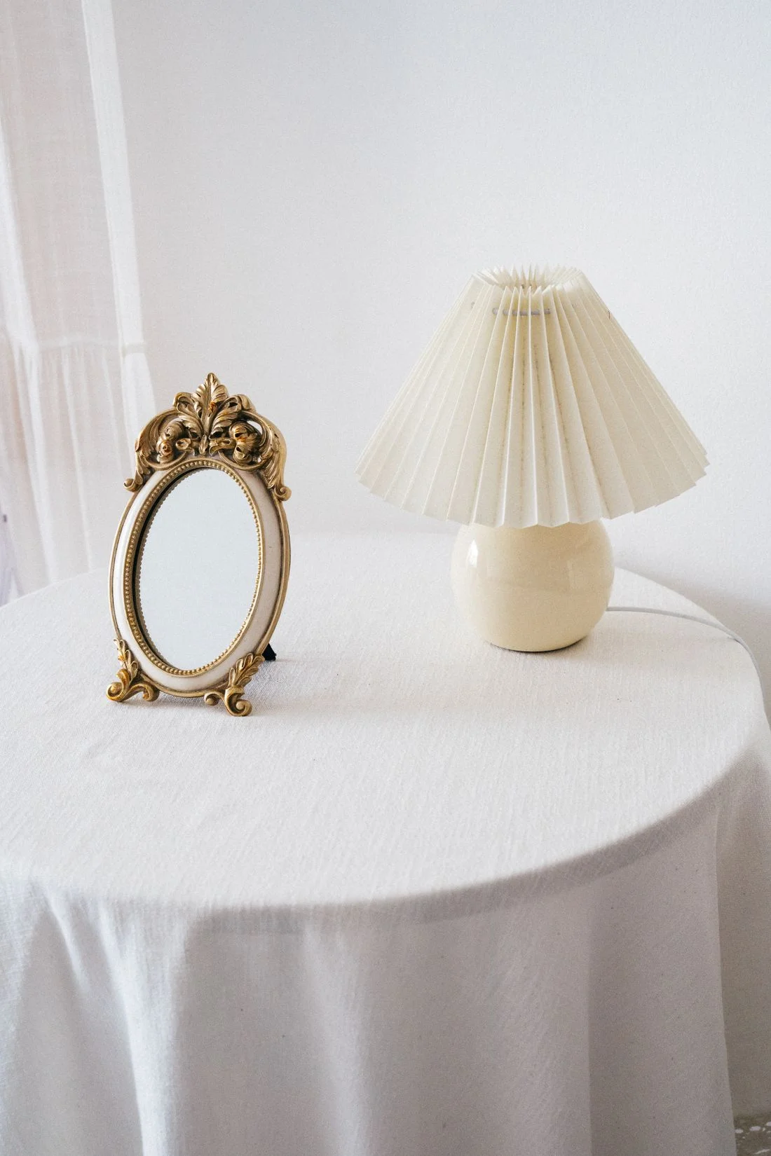 Pleated table lamp beside an ornate mirror